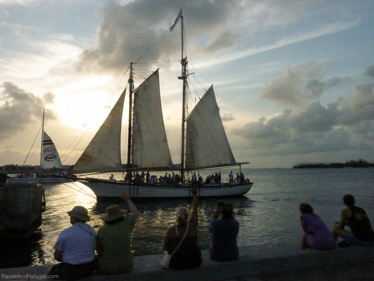 A boatload of tourists passes Mallory Square, where several thousand visitors watch performers as they wait for the 